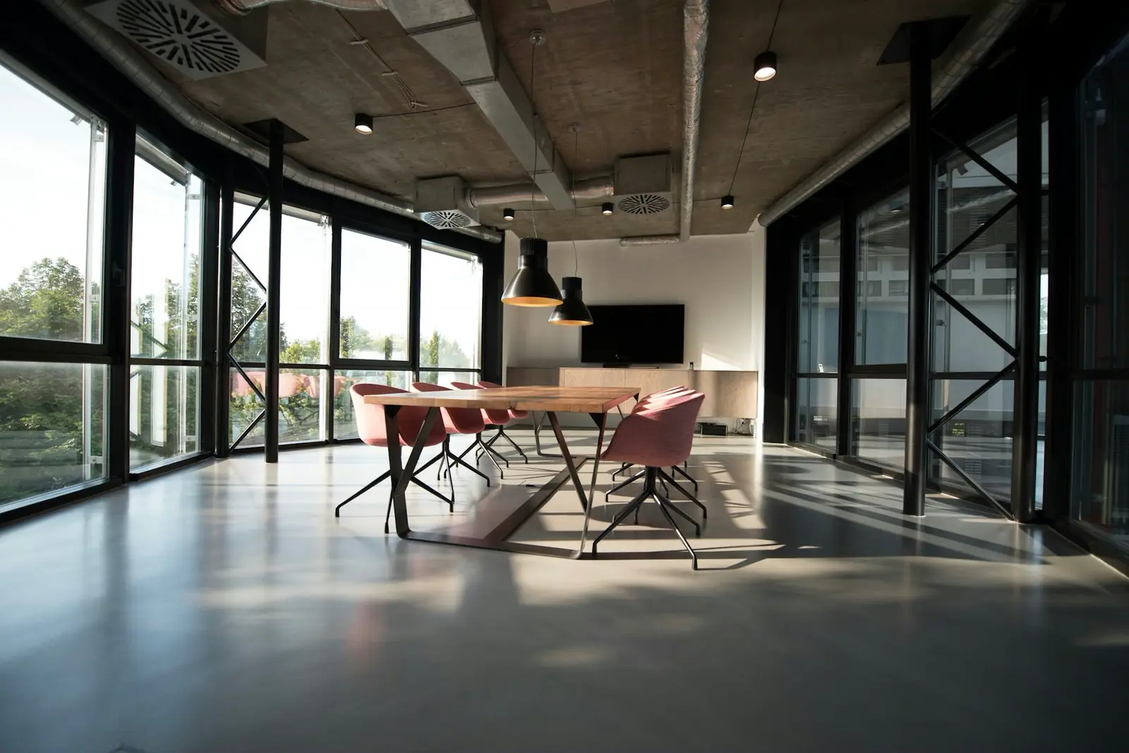 A glass-walled meeting room with a long wooden table in a bright office.